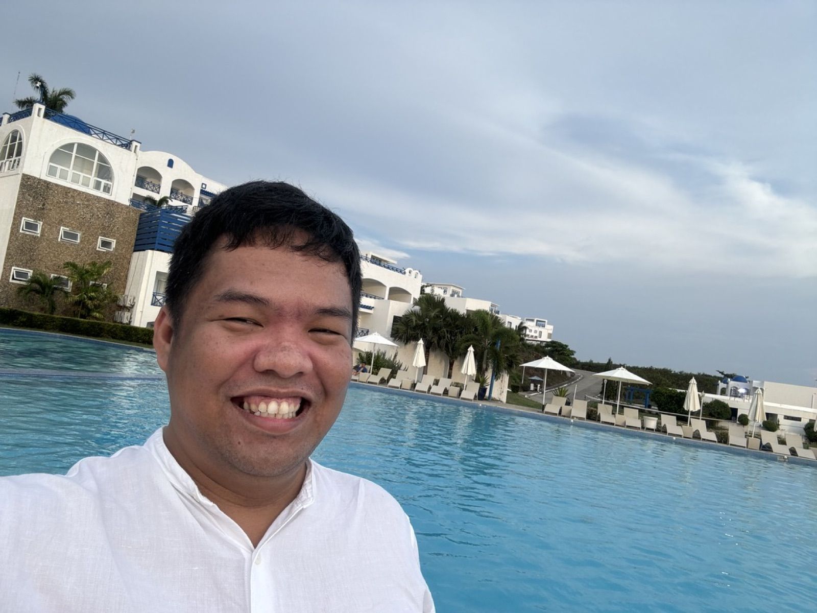 Allanaire smiling in a white shirt beside an infinity pool